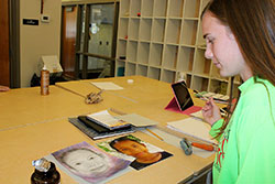 Bishop Chatard High School senior Kate Phelps pauses to examine her portrait of a Cambodian child before adding her final touches to the art work. (Submitted photo)